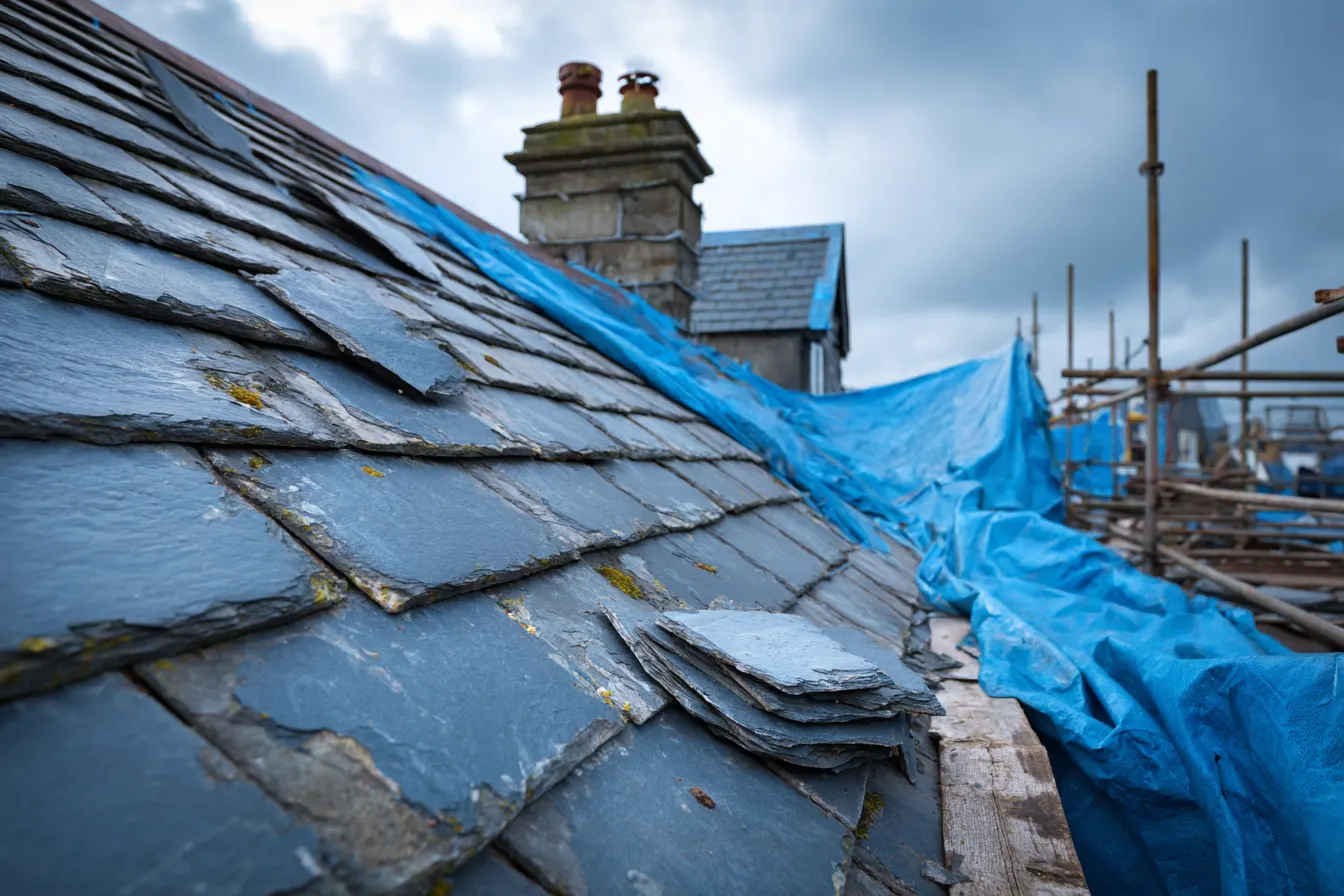 Storm damaged slate roof covered with a tarpaulin awaiting emergency roof repair